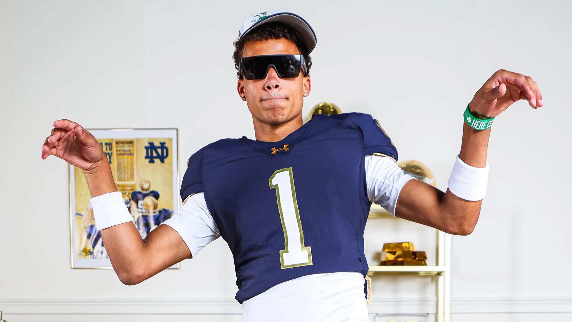 Portrait of Dylan Faison in a Notre Dame No. 1 football jersey wearing sunglasses and flexing with outstretched arms