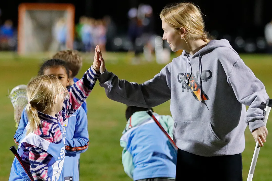A coach high fives a young girl during a lacrosse clinic