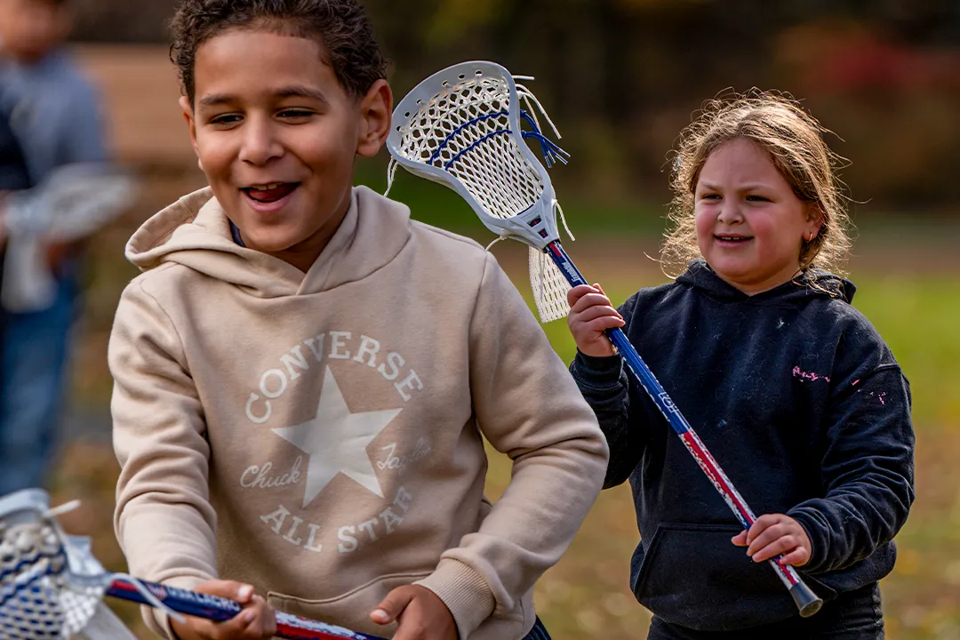 Young boy and young girl participate in lacrosse drills during a PE class