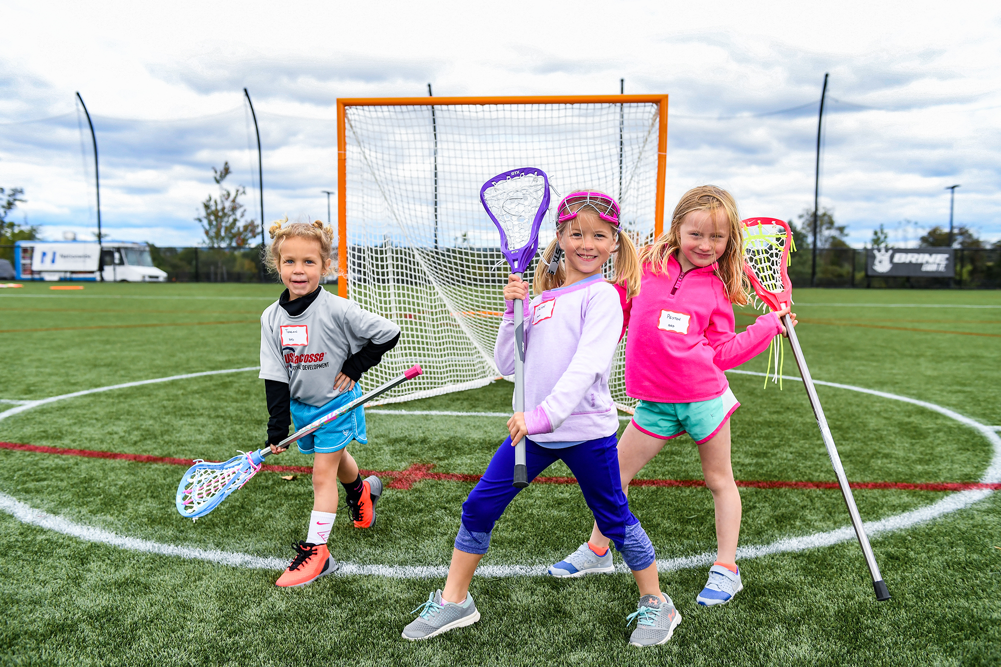 Young girls posing in front of the goal during a lacrosse clinic.