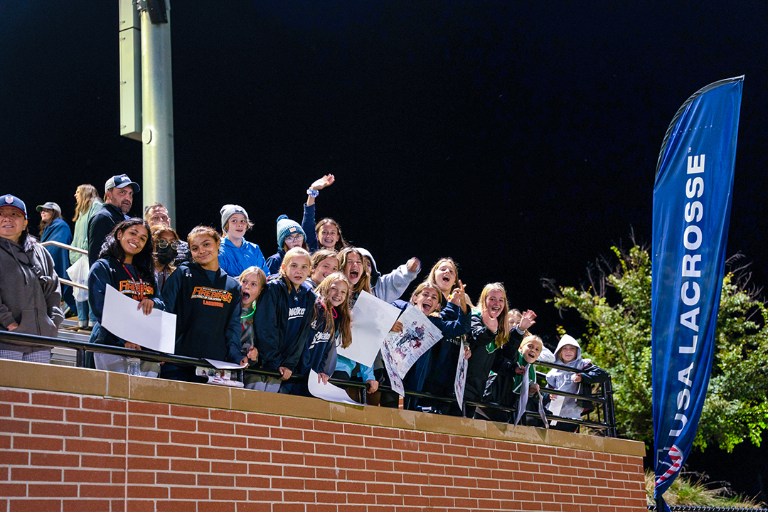 Fans in the stands with signs at USA Lacrosse's Tierney Field