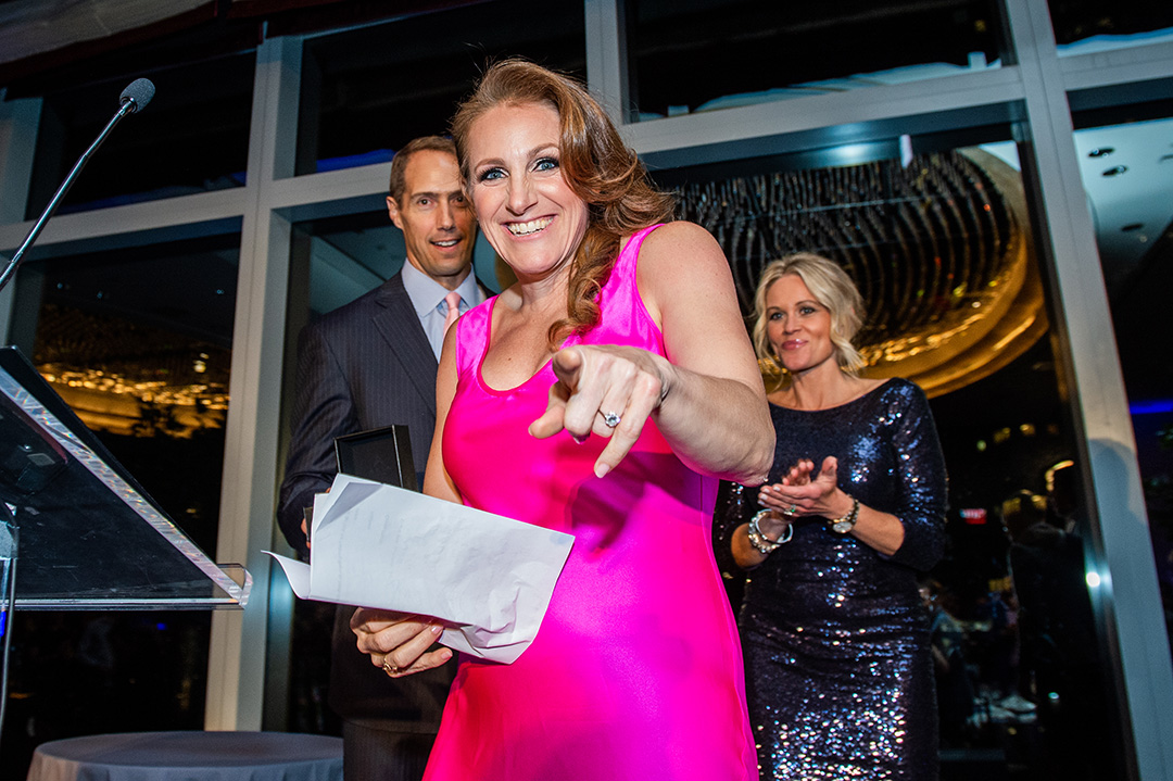 Crista Samaras points at the camera while wearing a pink dress as she is honored at the 2022 USA Lacrosse Foundation Gala