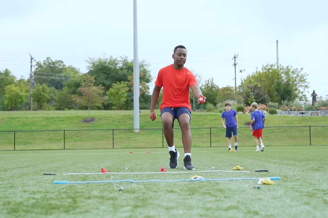 Lacrosse player tosses a bag into a hula hoop as part of warmup routine
