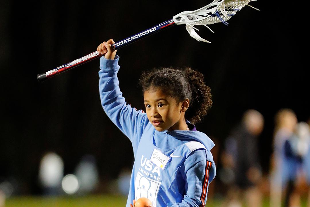 Youth girls lacrosse player holds a stick over her head at a USA Lacrosse clinic