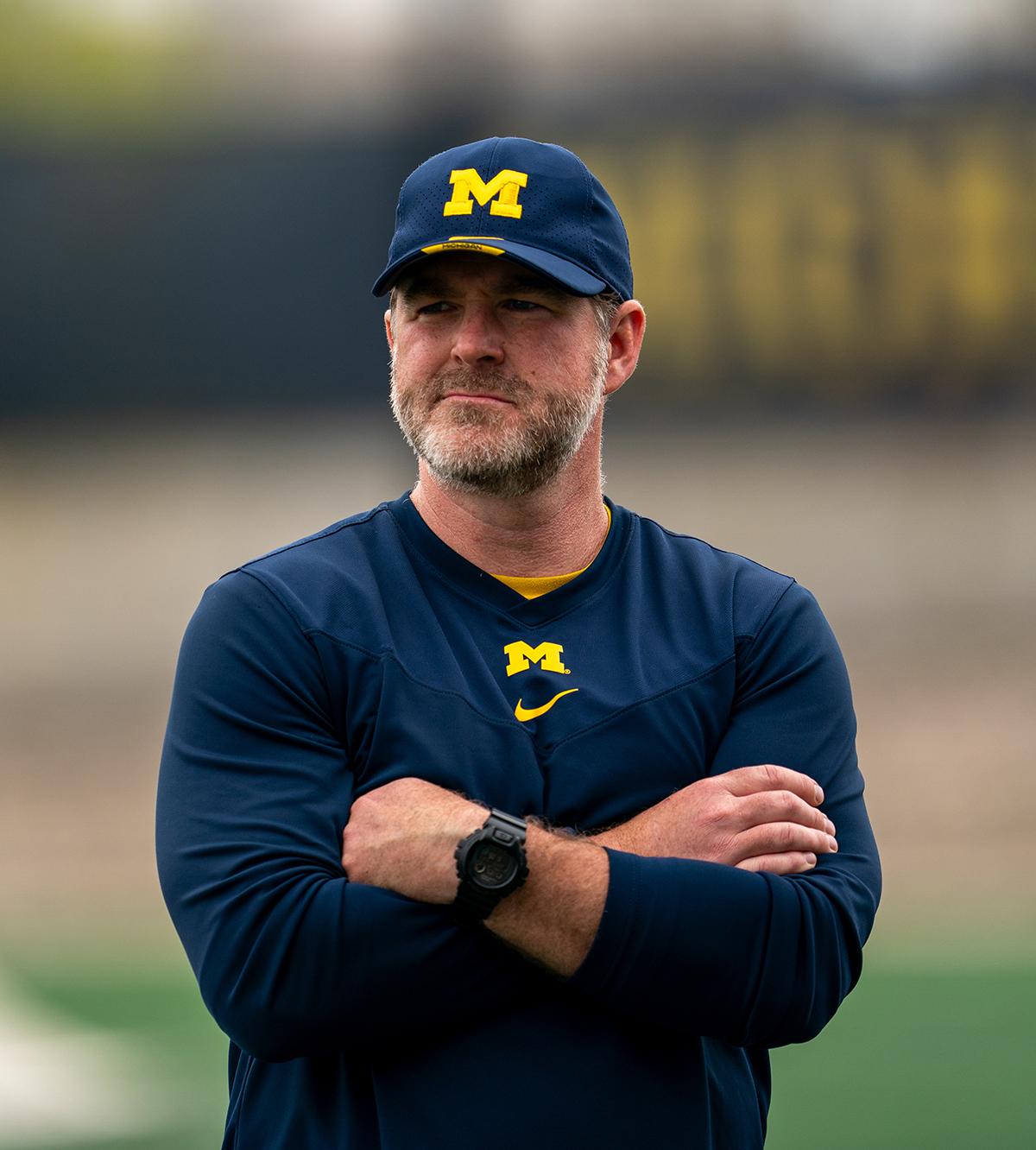 Michigan lacrosse coach Kevin Conry with arms folded on the sideline